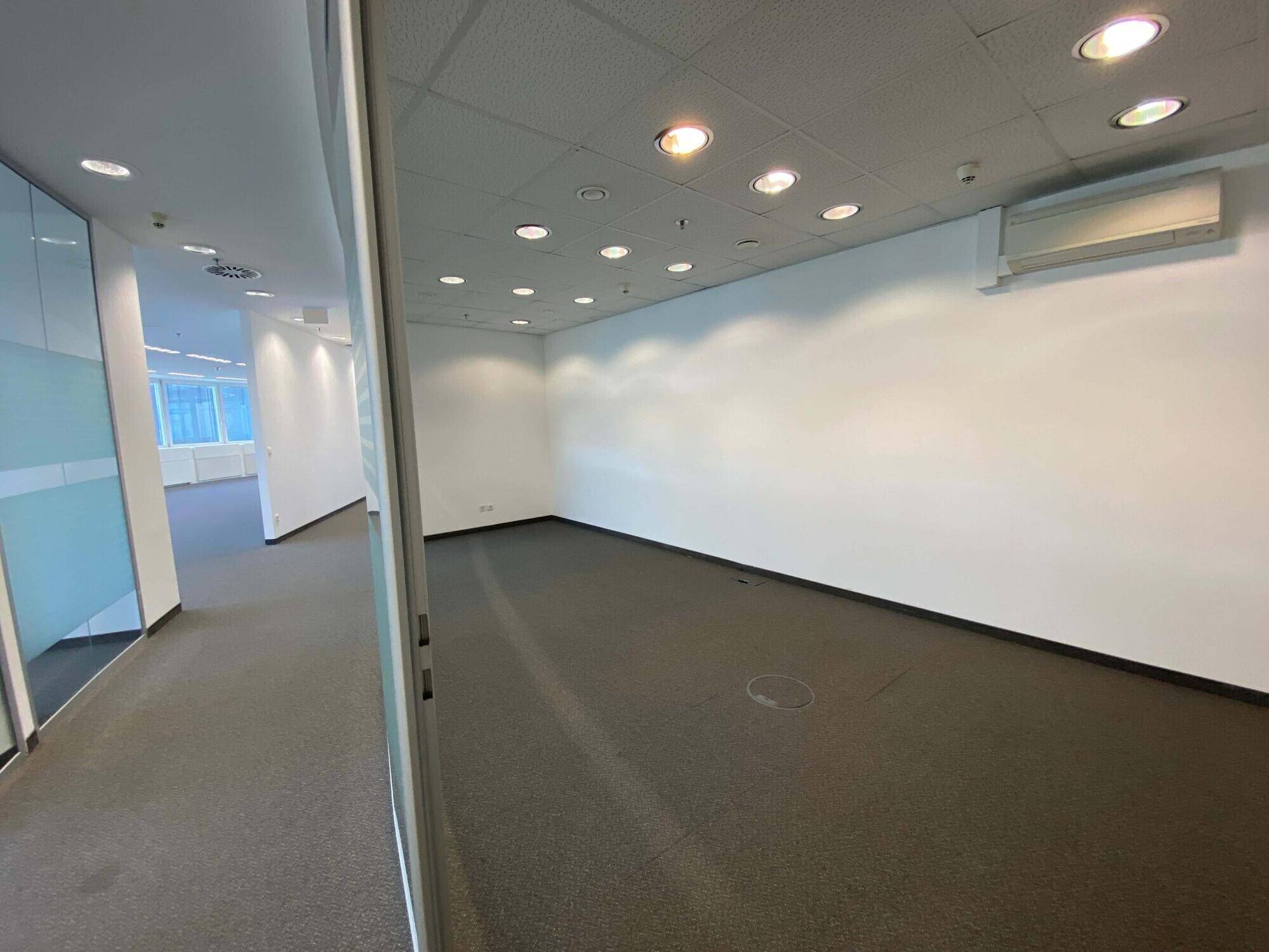 Moderner Bürogang mit Glaswänden und Teppichboden, der zu weiteren Büroräumen führt.