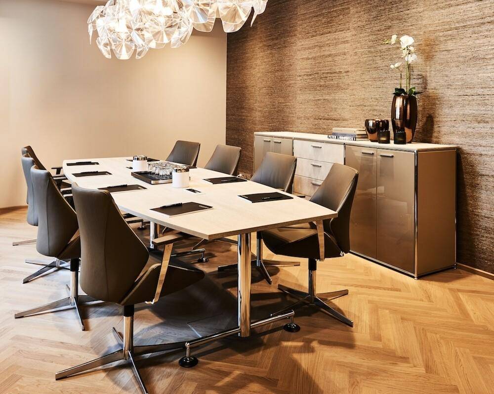 Heller Konferenzraum mit einem rechteckigen Tisch, bequemen Stühlen und einem auffälligen Kronleuchter.