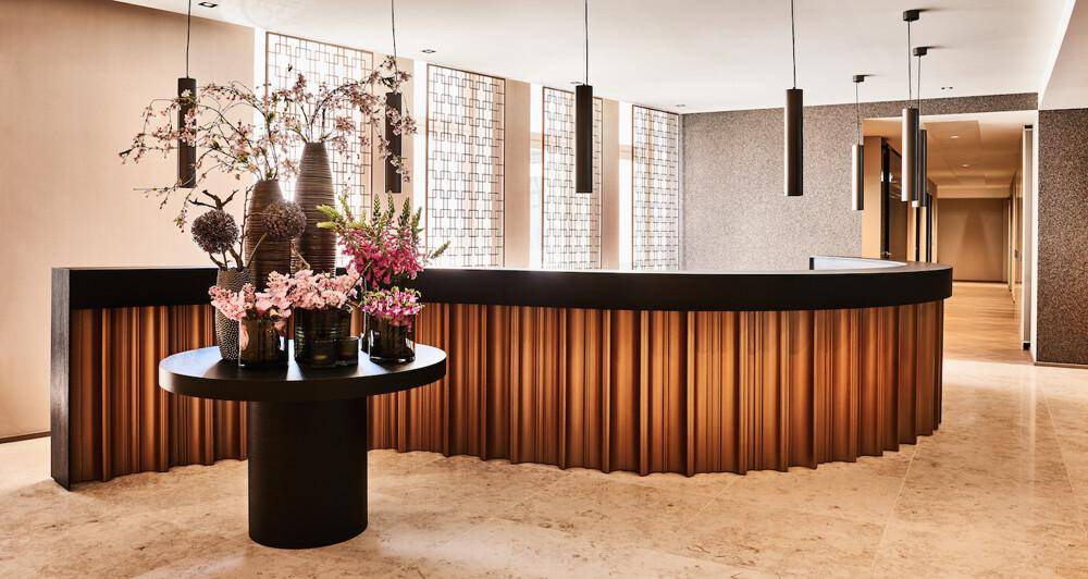 Elegante Empfangstheke mit Holzlamellen und floraler Dekoration in einem modernen Eingangsbereich.