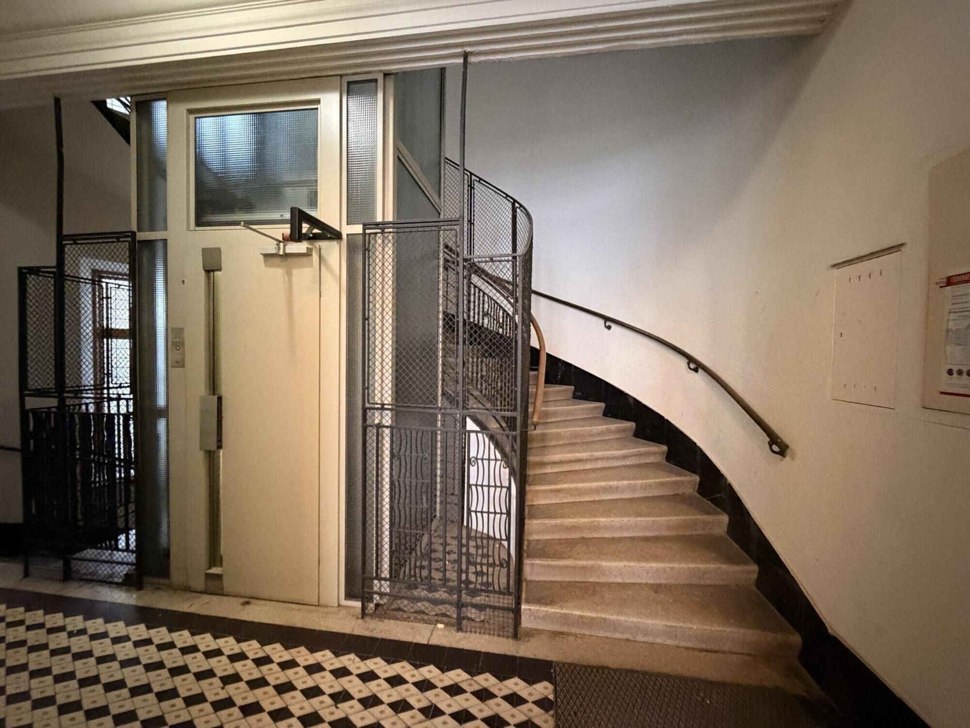 Historisches Treppenhaus mit geschwungener Treppe und einem Aufzug, der den Zugang zu den Etagen erleichtert.