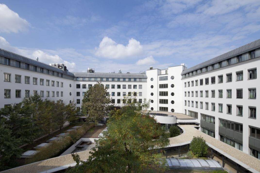 Grüner Innenhof, umgeben von einem großen Gebäude, mit Bäumen und angelegten Gartenbereichen.