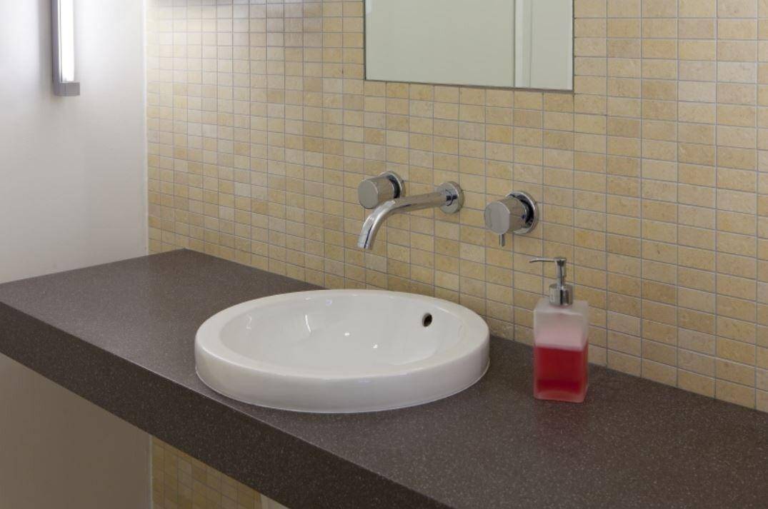 Modernes Badezimmer mit einem runden Aufsatzwaschbecken, Wandarmatur und beigen Mosaikfliesen.