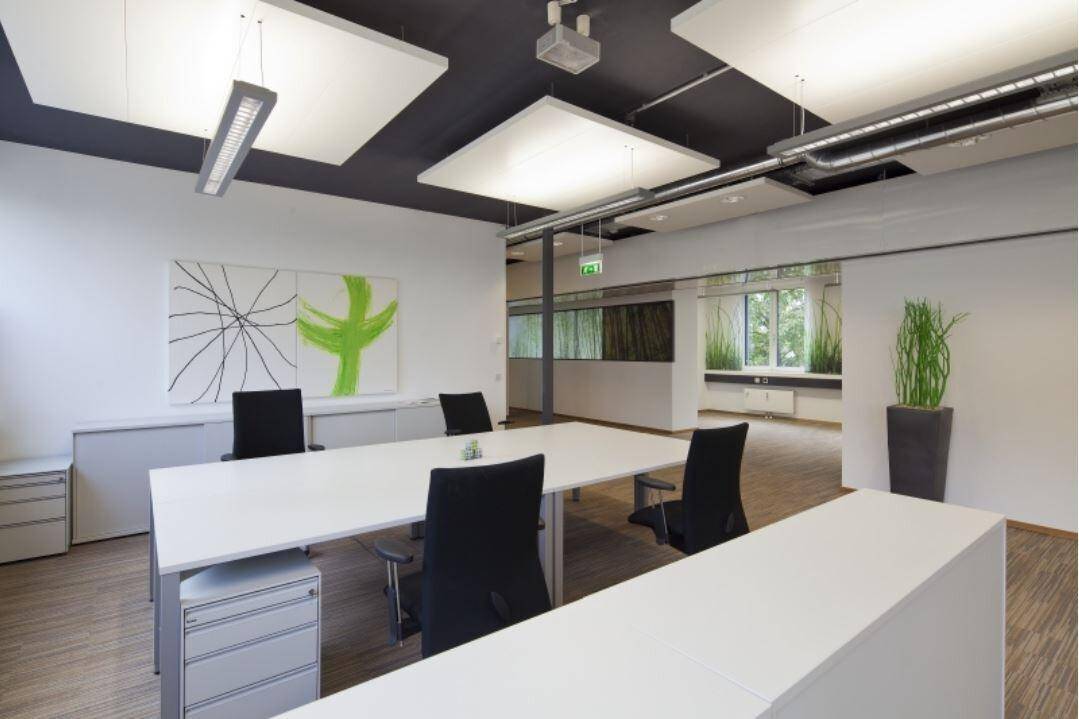 Modernes und helles Büro mit mehreren Arbeitsplätzen, ergonomischen Stühlen und schallabsorbierenden Deckenplatten.