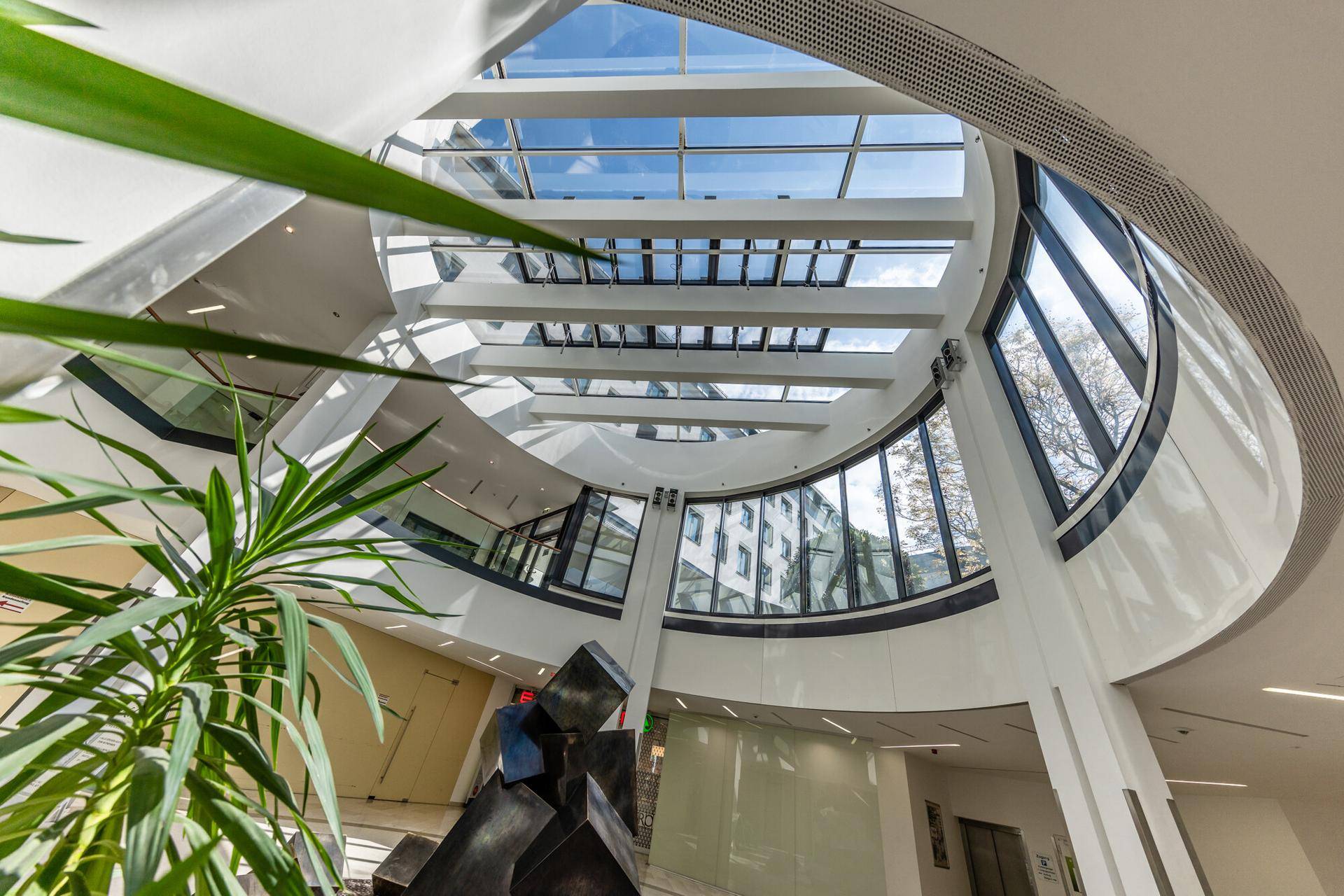 Beeindruckendes, modernes Atrium mit Glasdach und großen Fenstern, das viel natürliches Licht hereinlässt.