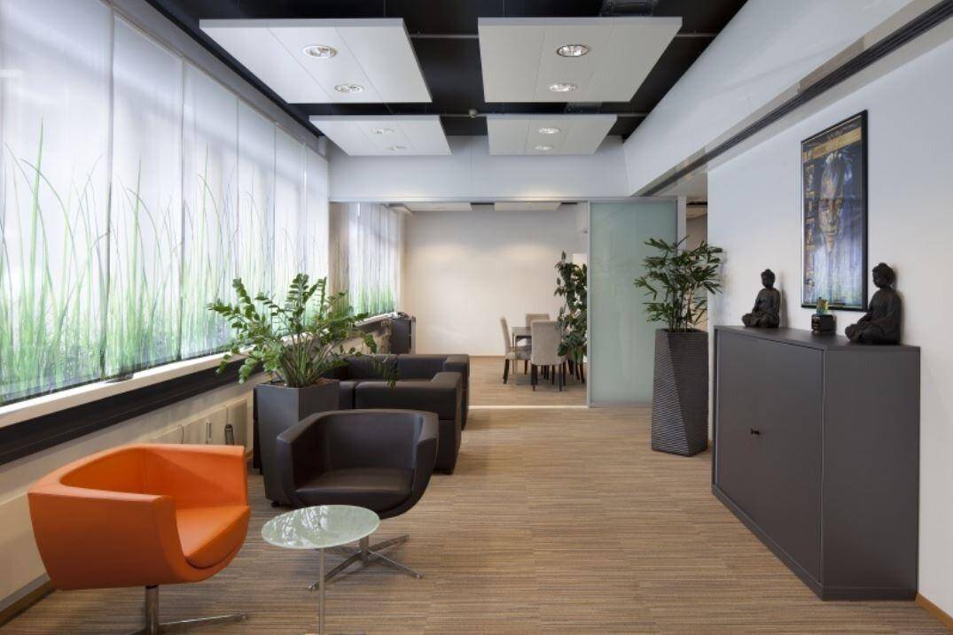 Moderner Büroloungebereich mit bequemen Sesseln, Pflanzen und Blick in einen angrenzenden Konferenzraum.