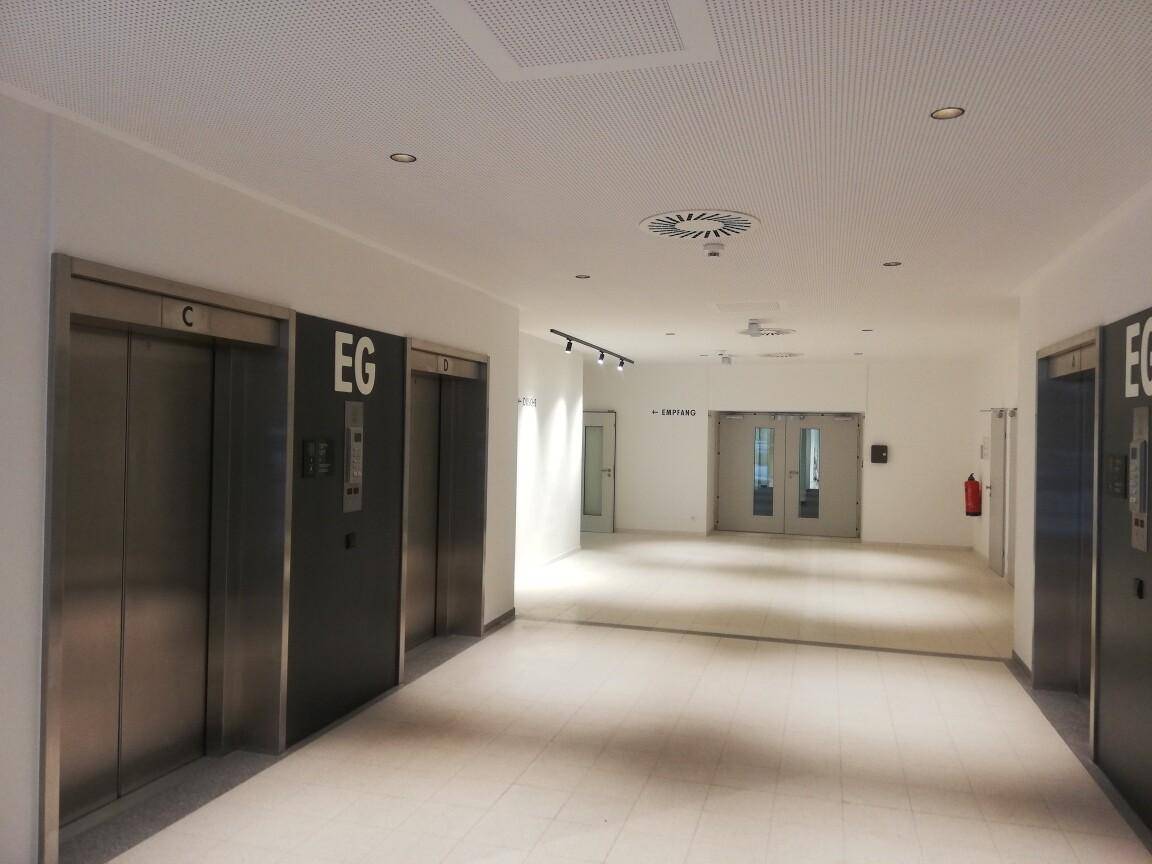 Weitläufiger Flur mit Aufzügen und einem Eingangsbereich, der zu weiteren Räumlichkeiten führt.