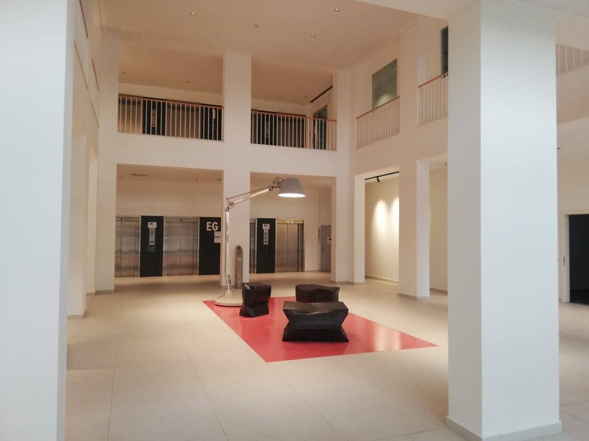 Großzügige Lobby mit Design-Sitzmöbeln, einer markanten Stehlampe und Aufzügen im Hintergrund.