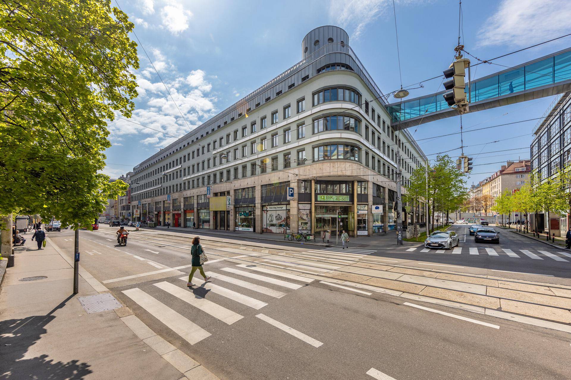 Großes, modernes Gebäude mit geschwungener Fassade an einer belebten Straßenkreuzung in der Stadt.
