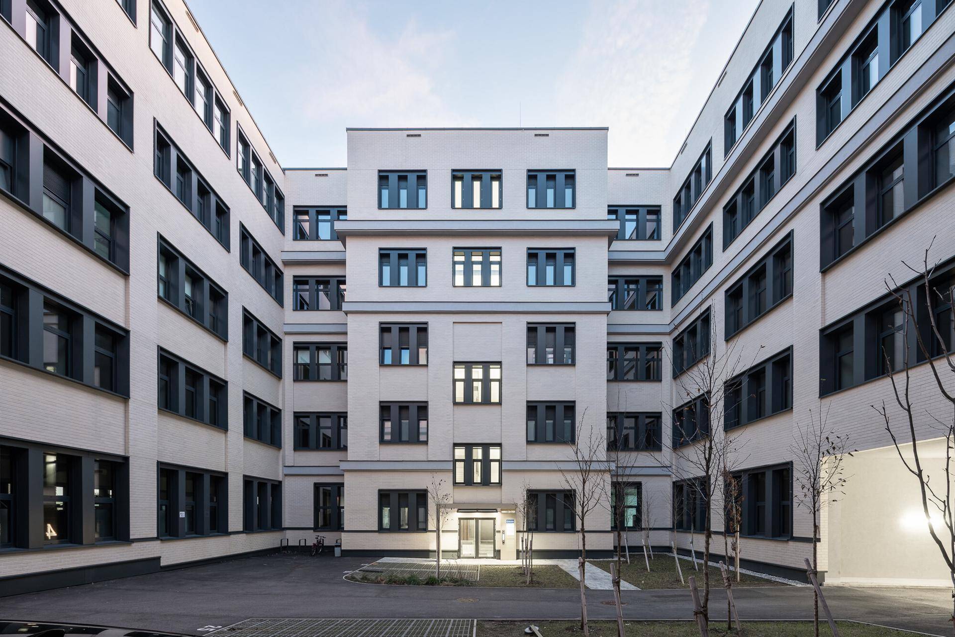 Moderne Gebäudefassade mit vielen Fenstern, die einen Innenhof umgibt und eine klare Architektur zeigt.