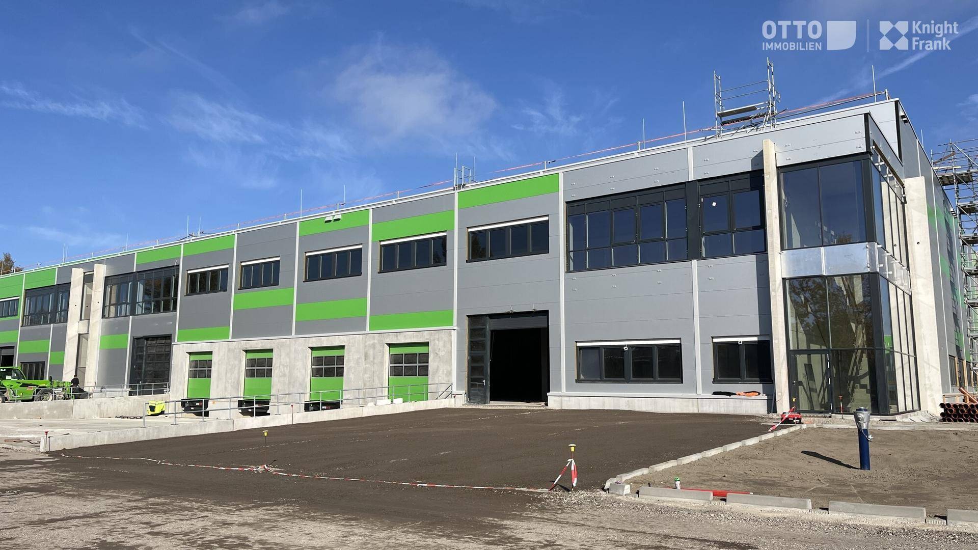 Moderne Fassade eines neuen Industriegebäudes mit großen Fenstern und grünen Akzenten.