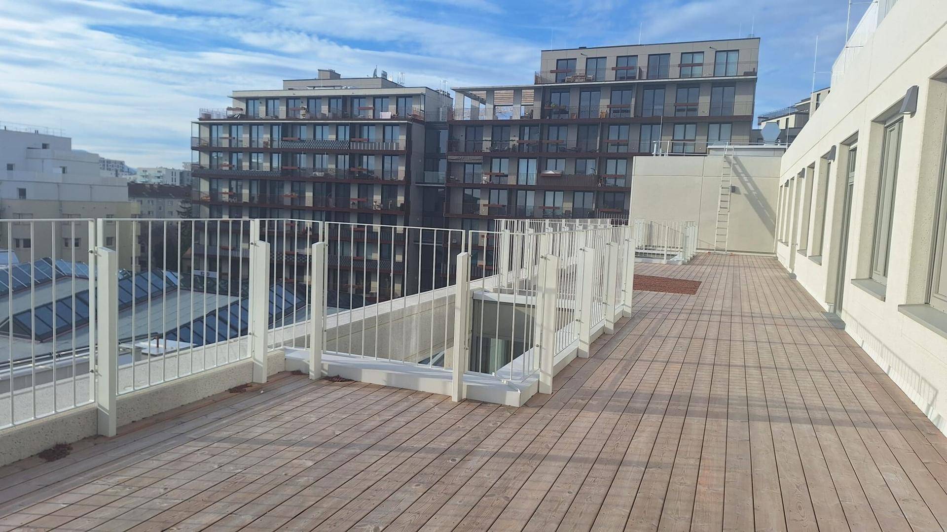 Geräumige Dachterrasse mit Holzbelag und weißem Geländer, bietet einen weiten Blick über die Stadtlandschaft.