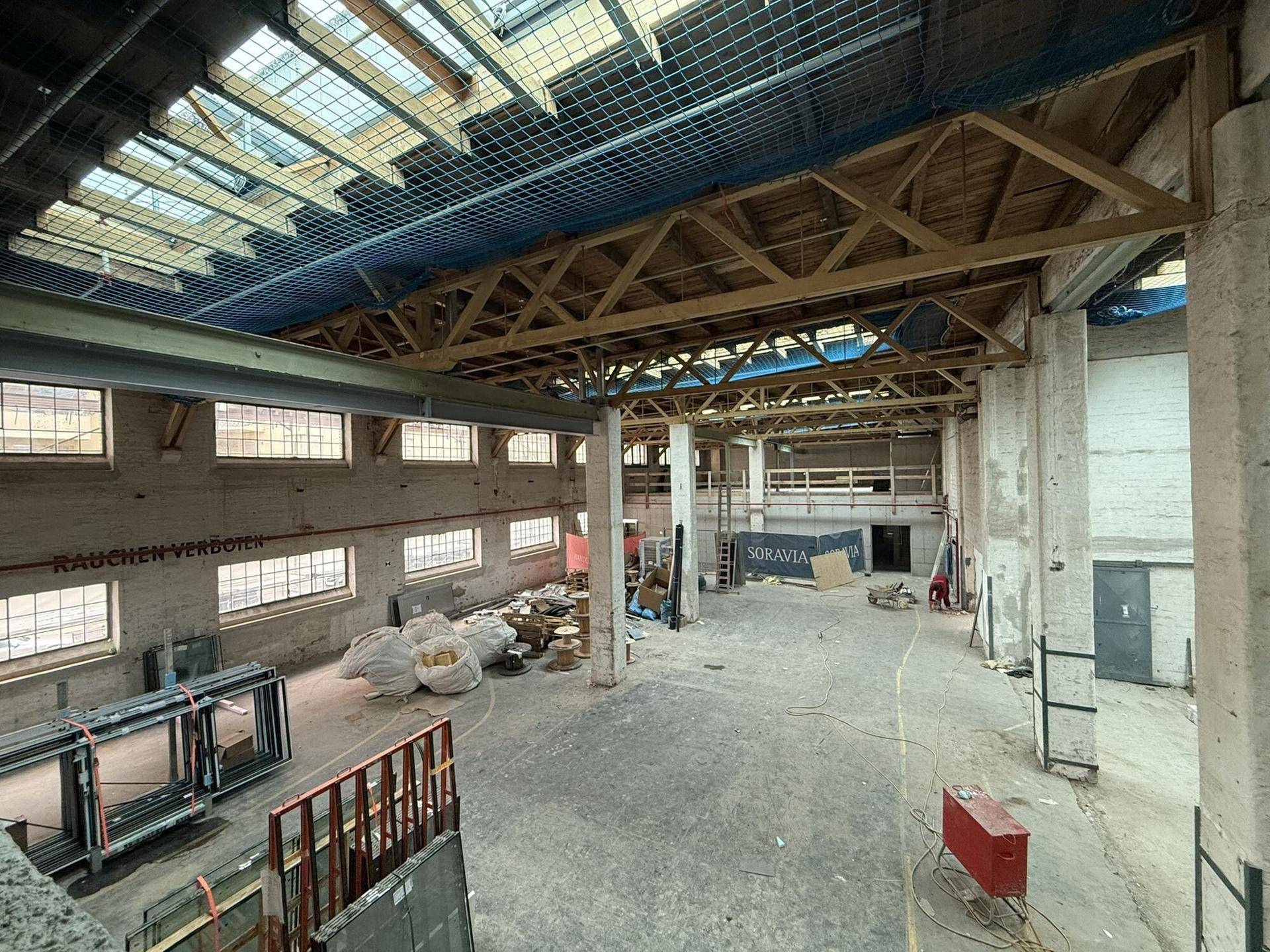 Geräumige Industriehalle mit hohen Decken, Oberlichtern und Baumaterialien, bereit für den Ausbau.