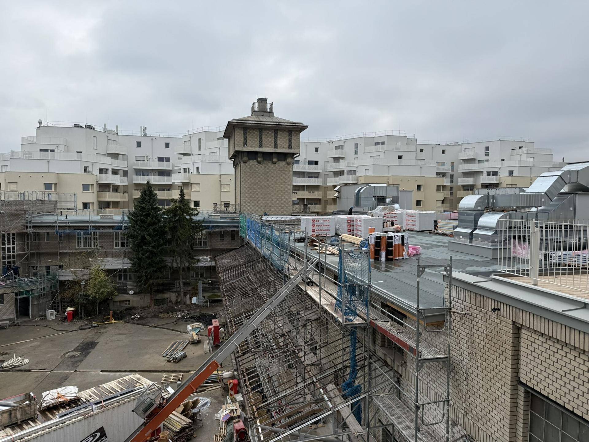 Blick über Dächer und Gebäudekomplexe mit einem alten Wasserturm und Baustellenaktivitäten.