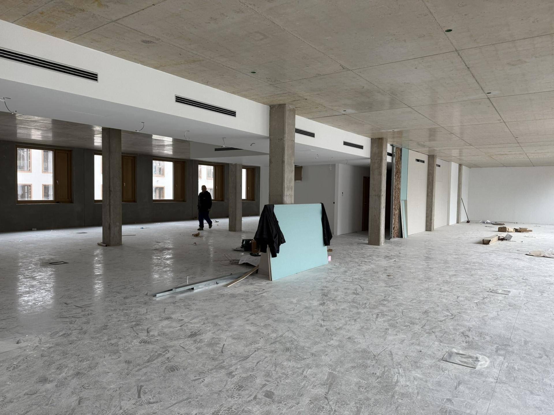 Großer, offener Büroraum im Rohbau mit Betonpfeilern, hohen Decken und vielen Fenstern.