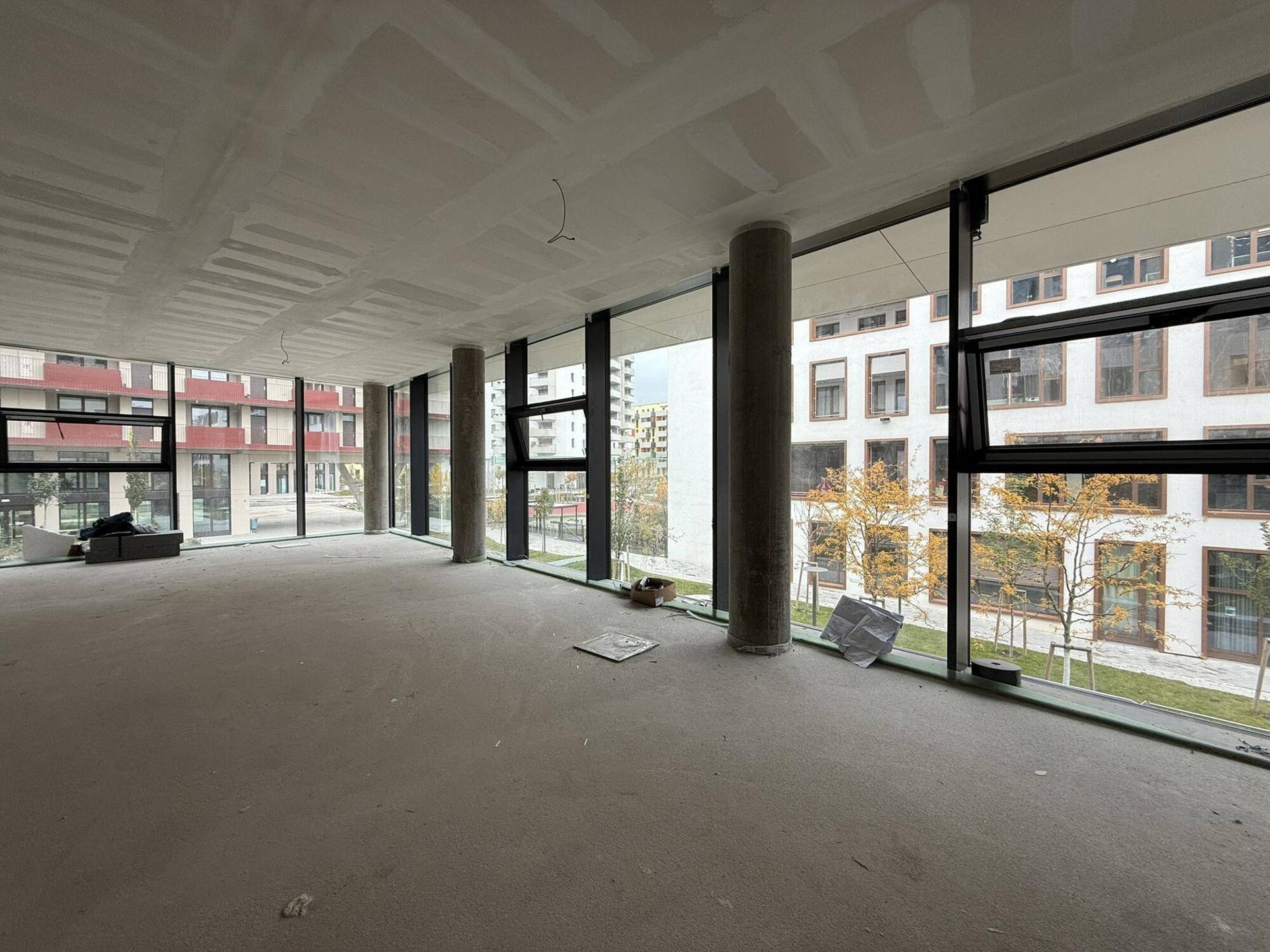 Großer, offener Raum mit raumhohen Fenstern und runden Betonpfeilern, noch im Rohbau.