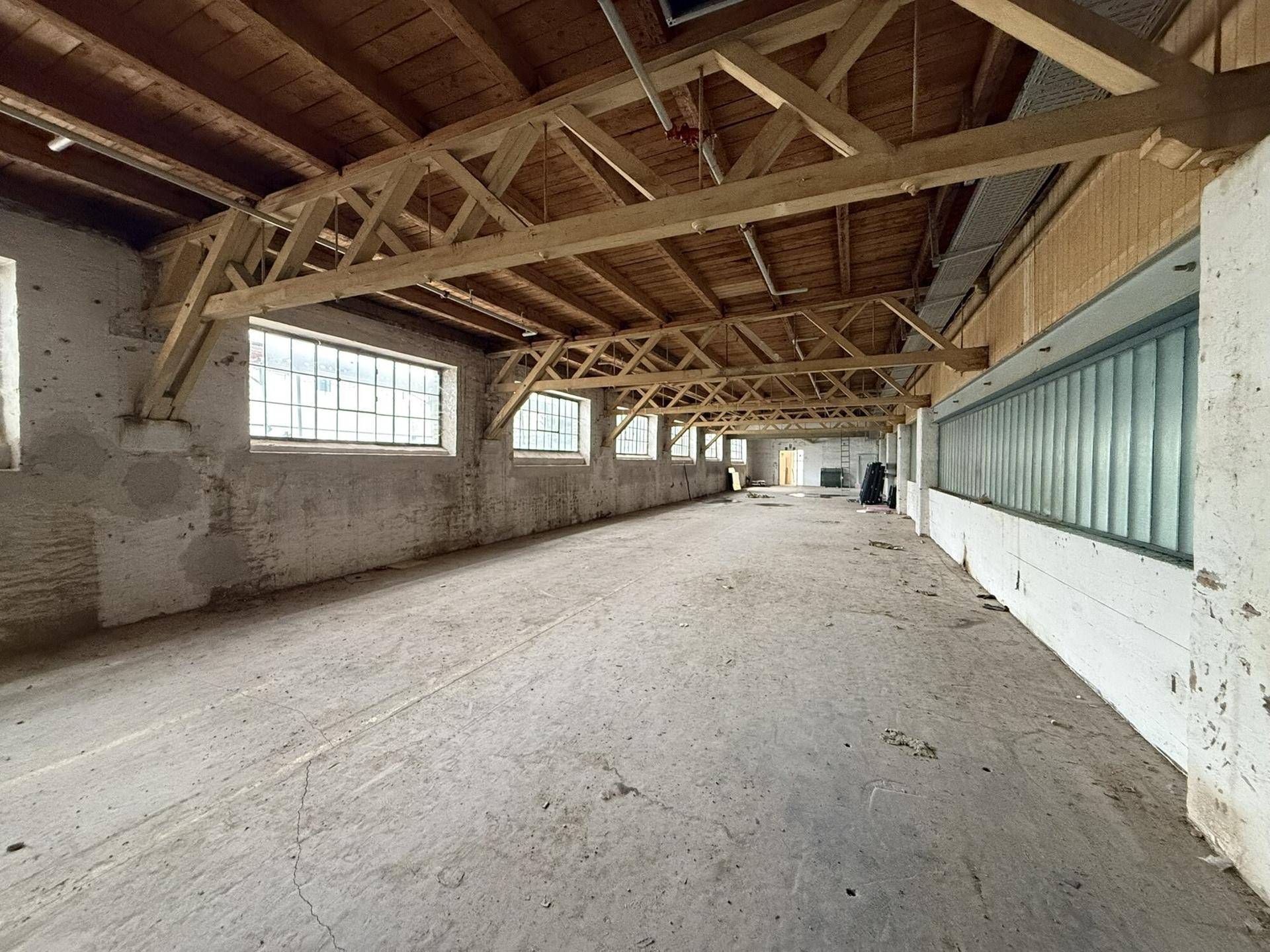 Großer, leerer Raum mit Holzbalkenkonstruktion und vielen Fenstern, ideal für gewerbliche Nutzung.