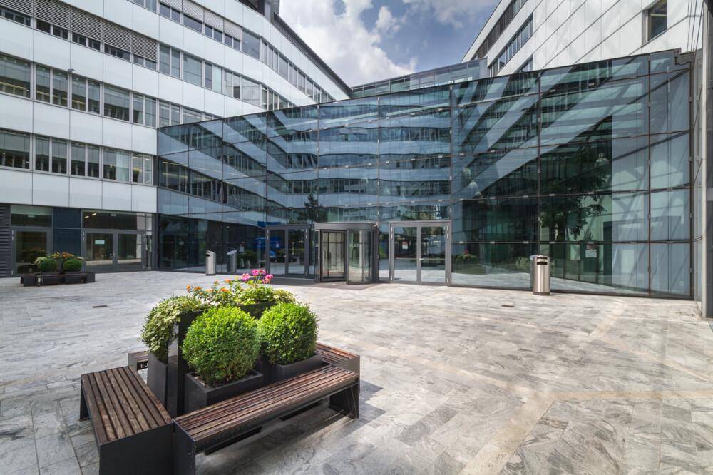 Innenhof eines modernen Bürokomplexes mit Glasfassade, Sitzgelegenheiten und Pflanzen.