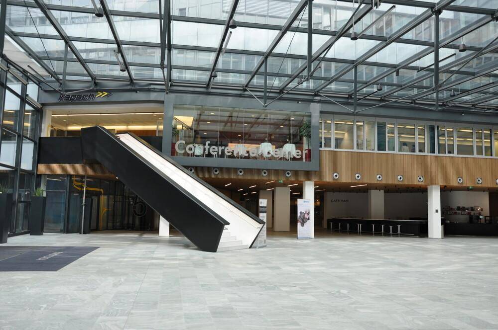 Geräumige Lobby mit Rolltreppe, Konferenzzentrum und Café-Bereich im Hintergrund.