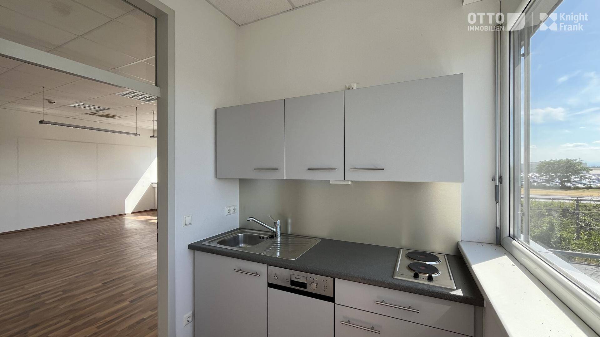 Kleine Küchenzeile mit grauen Schränken, Spüle und Kochfeld, direkt neben einem Fenster gelegen.