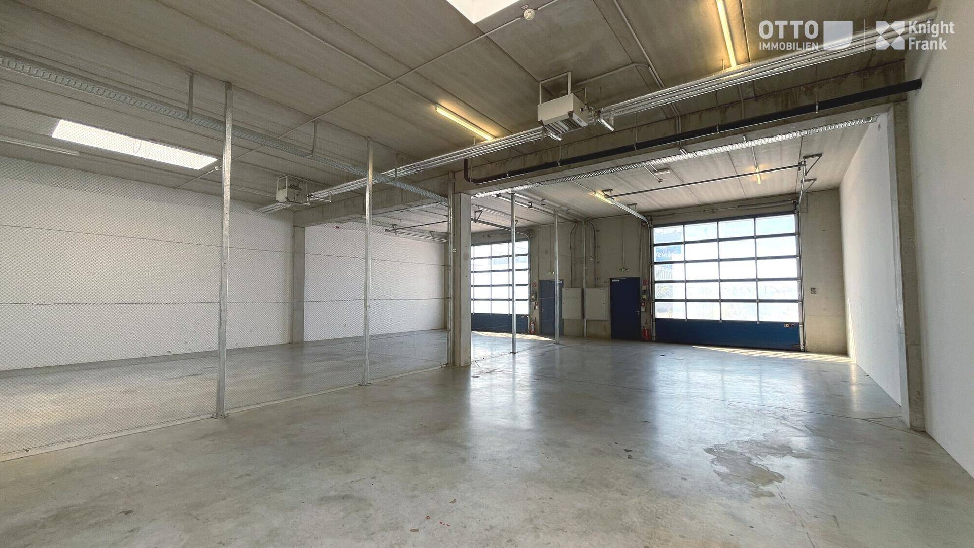 Geräumige Lagerhalle mit Betonboden, Oberlichtern und mehreren Rolltoren für den Zugang.