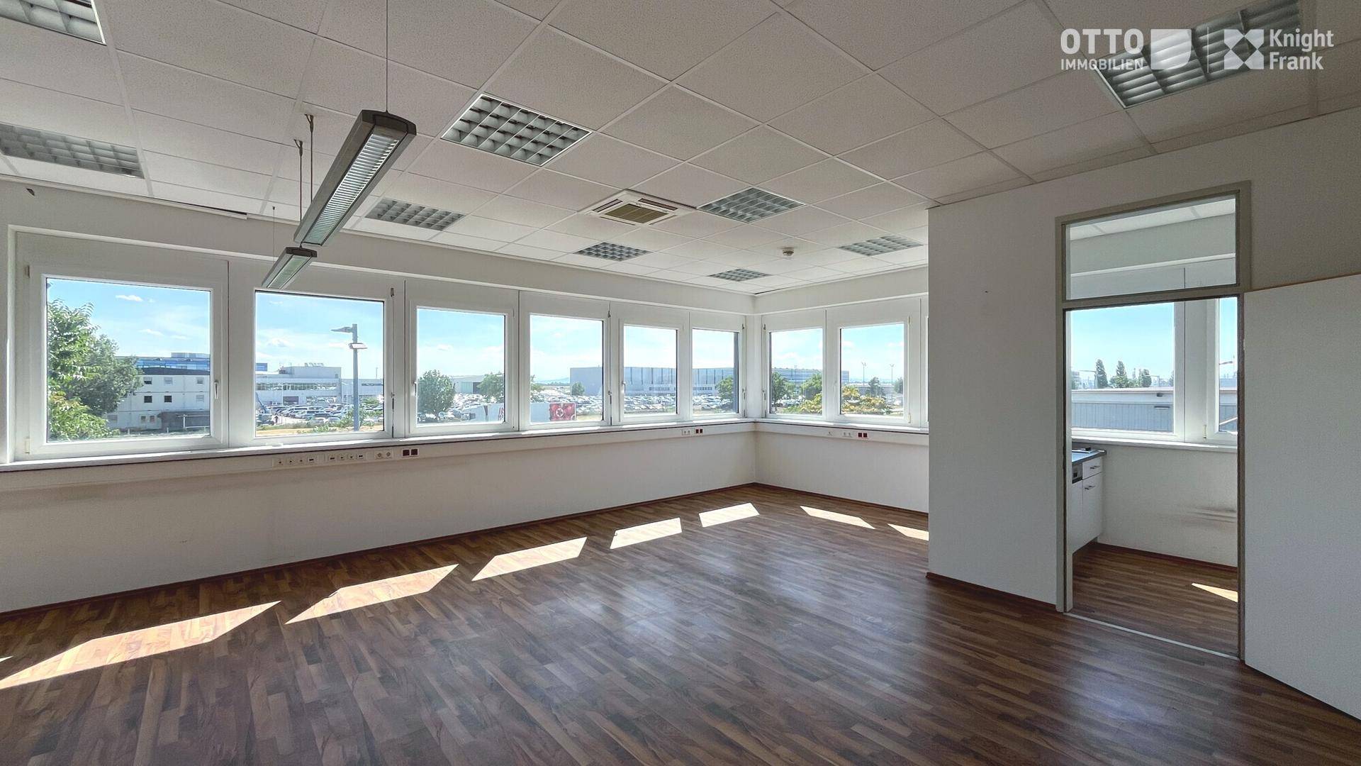 Heller Büroraum mit Laminatboden und einer Fensterfront, die den Blick nach draußen freigibt.