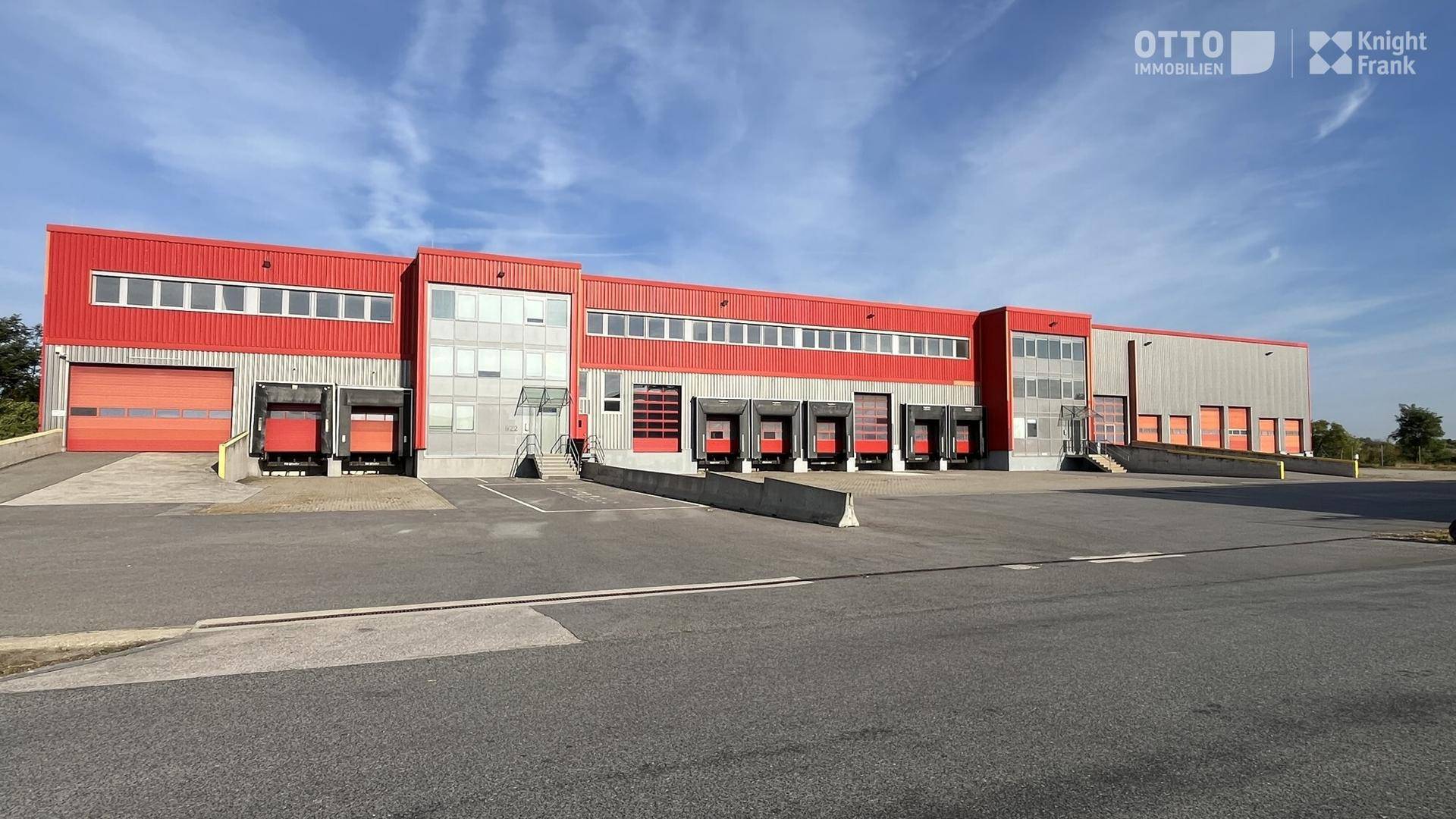 Ansicht der modernen Industriehalle mit zahlreichen Laderampen und roter Fassadenverkleidung unter blauem Himmel.