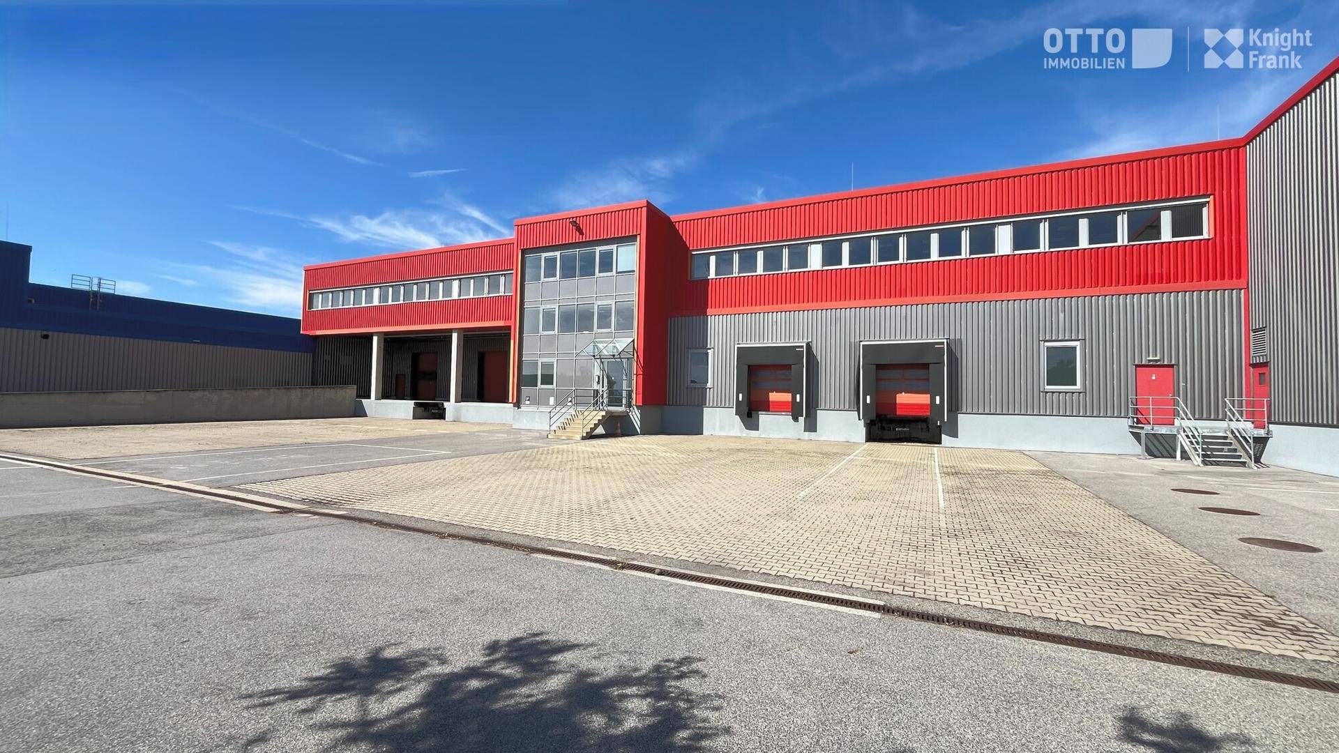 Gewerbegebäude mit roter und grauer Fassade, mehreren Laderampen und großem Vorplatz.