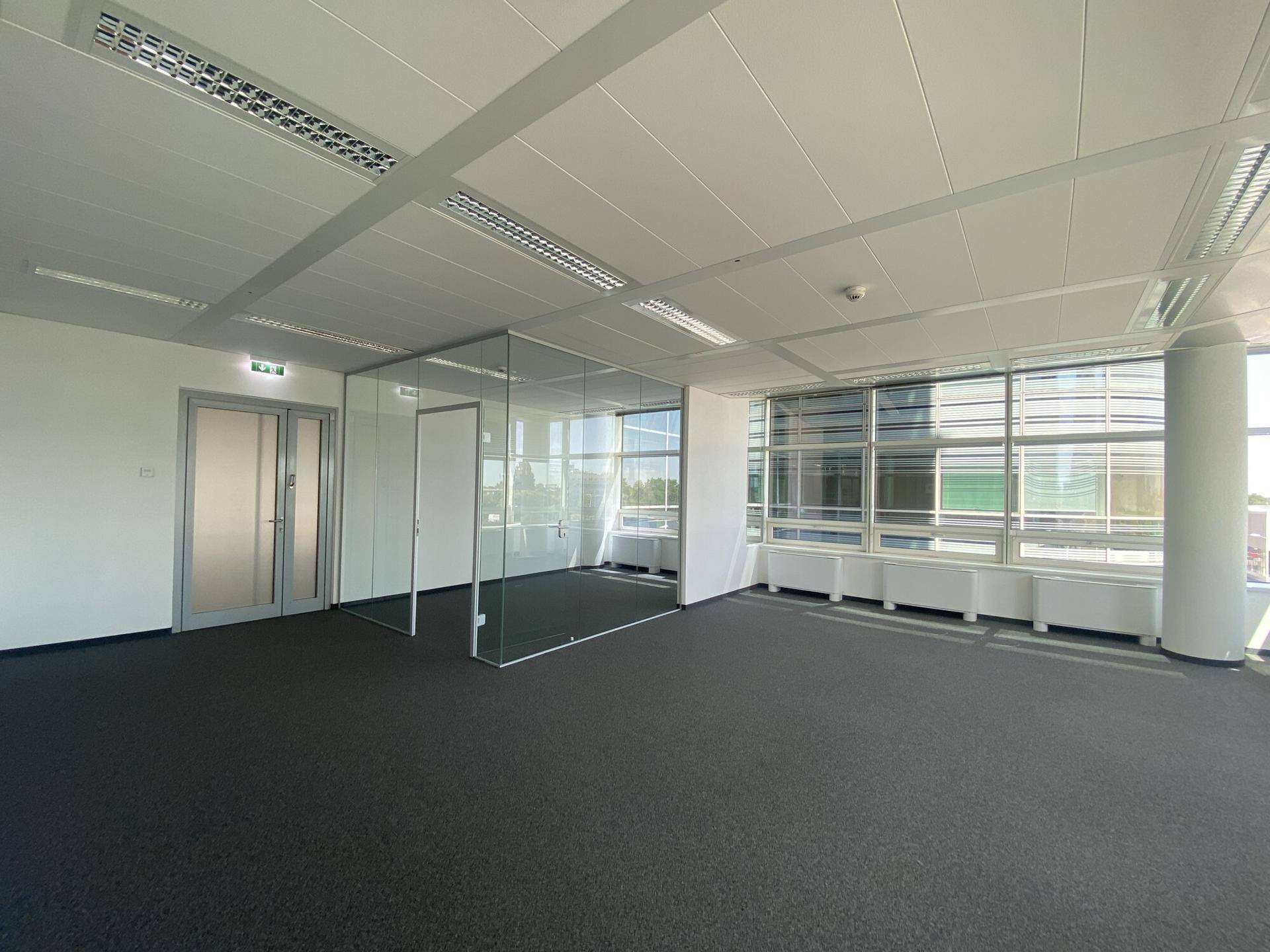 Moderner Büroraum mit Teppichboden, Glaswänden und viel Tageslicht durch große Fenster.