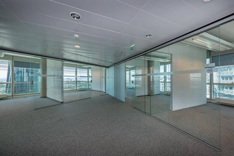 Offener Bürobereich mit Glasabtrennungen, die separate Büros schaffen, und großen Fenstern.