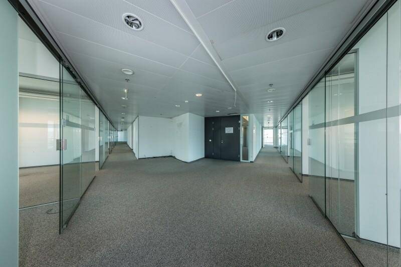 Langer Bürogang mit beidseitigen Glasbüros, Teppichboden und moderner Deckenbeleuchtung.