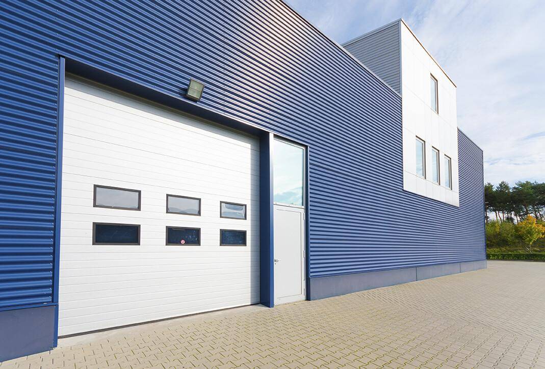 Moderne Industriefassade in Blau mit großem Sektionaltor und seitlichem Eingangsbereich.