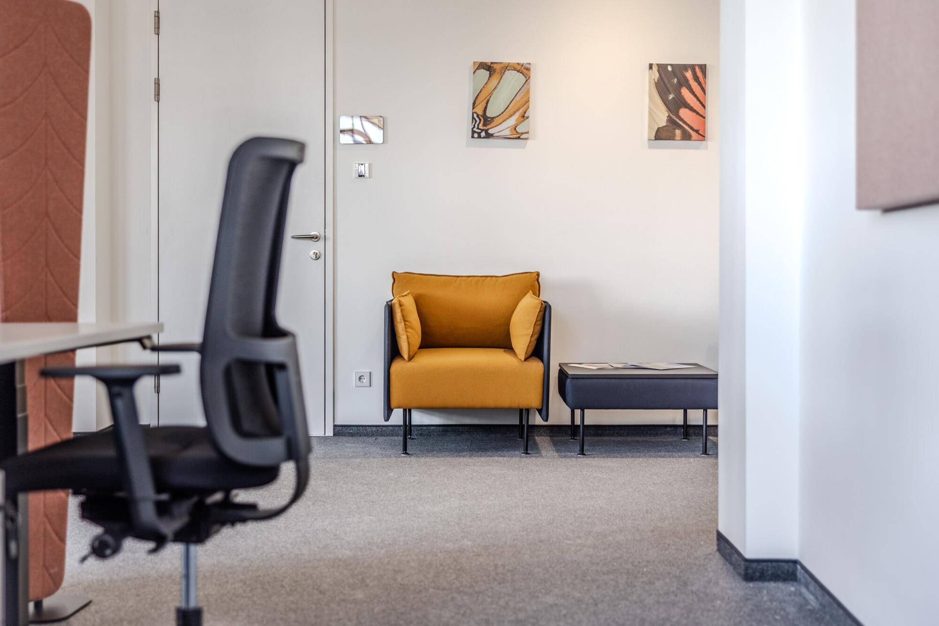 Einladender Wartebereich in einem modernen Büro mit gelbem Sessel, Kunst an der Wand und Teppichboden.