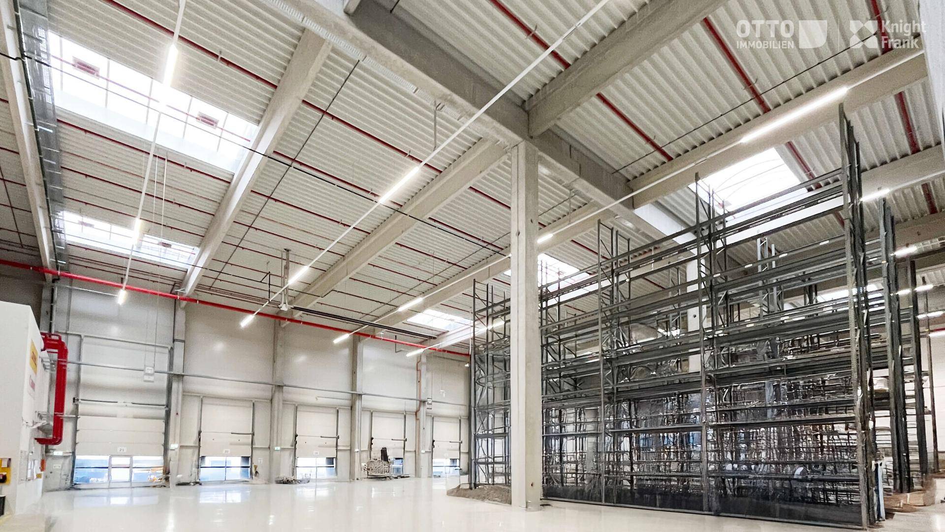 Weitläufige Lagerhalle mit hohen Regalsystemen, Rolltoren und viel Tageslicht durch Oberlichter.