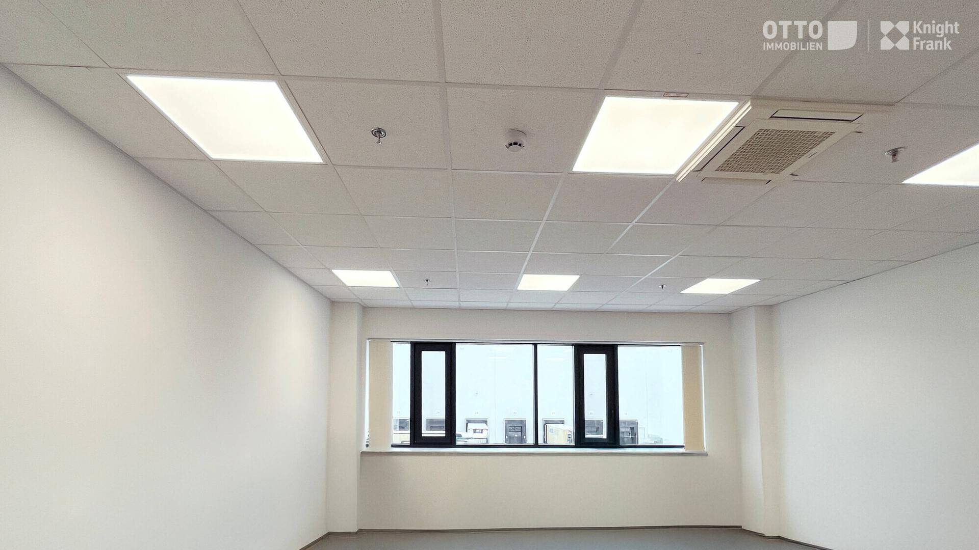 Helles Büro mit abgehängter Decke, integrierter Beleuchtung und breiten Fenstern für Tageslicht.