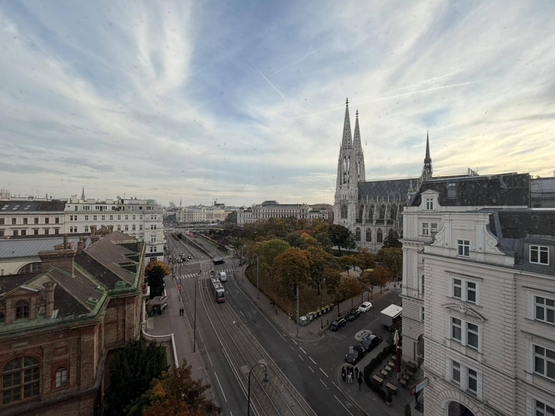 Panoramablick über eine belebte Stadtstraße mit historischer Kirche und umliegenden Gebäuden unter bewölktem Himmel.