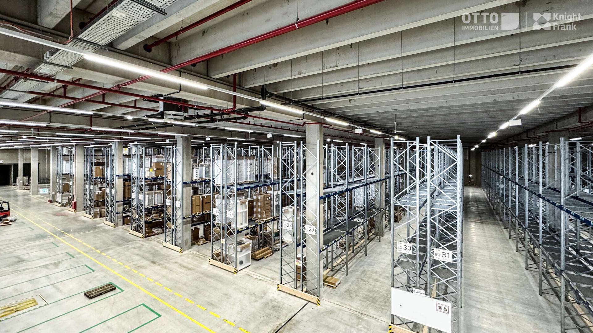 Blick von oben auf die Lagerregale mit verpackten Waren und breiten Gängen in der Halle.