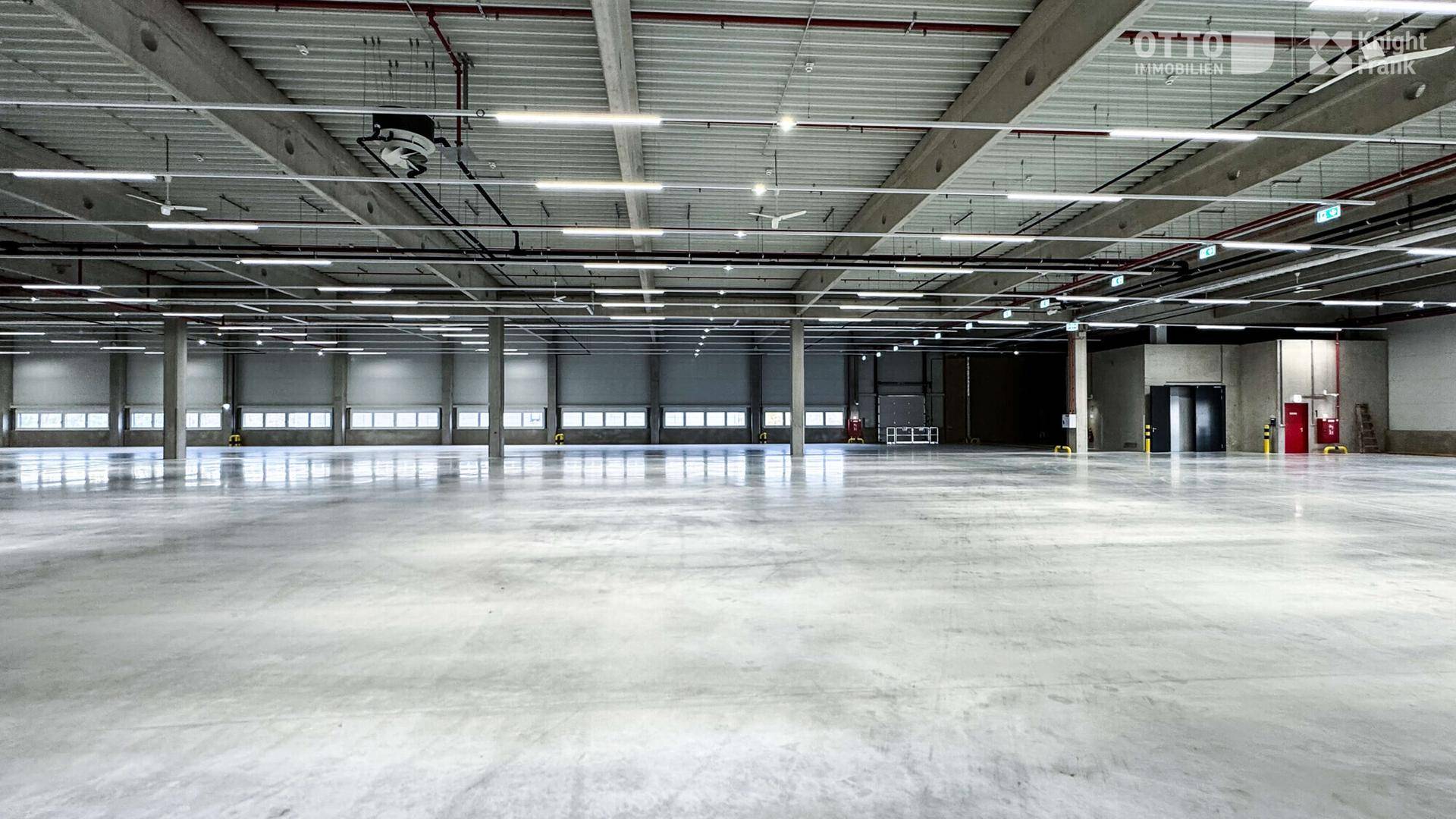 Große, leere Lagerhalle mit vielen Rolltoren, hohen Decken und Deckenventilatoren für Belüftung.