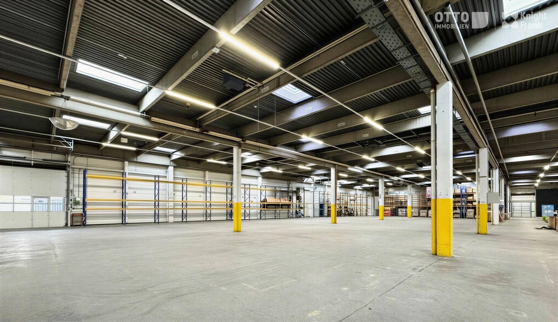 Weitläufige Lagerhalle mit hohen Decken, Betonboden und gelben Stützpfeilern.