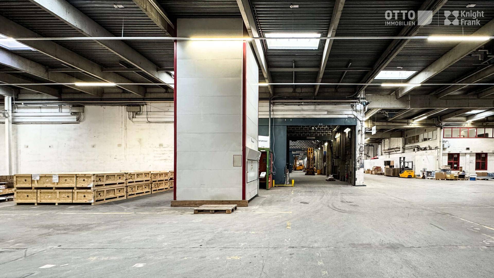 Große Lagerhalle mit Betonboden, hohen Decken und einigen Holzkisten im Vordergrund.