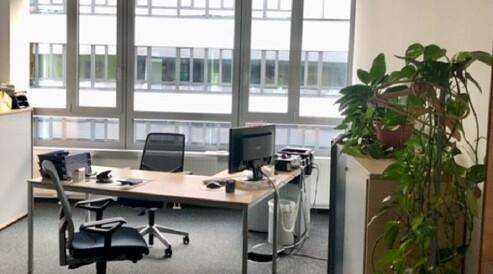 Helles Einzelbüro mit Schreibtisch, Bürostühlen und großen Fenstern mit Blick auf andere Gebäude.