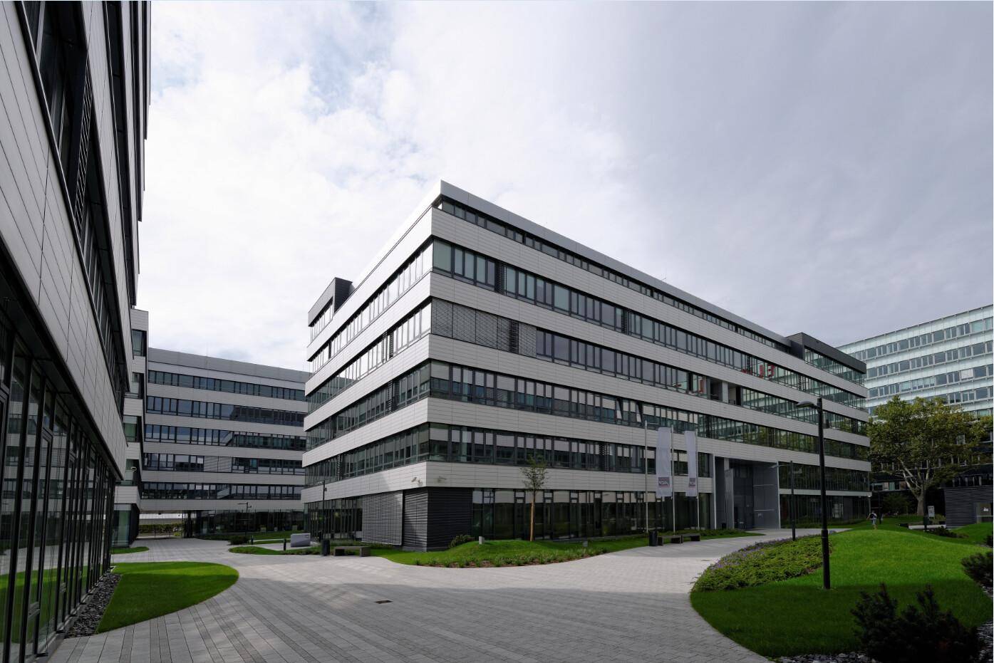 Mehrere moderne Bürogebäude mit großen Fensterflächen und einem begrünten Innenhof.
