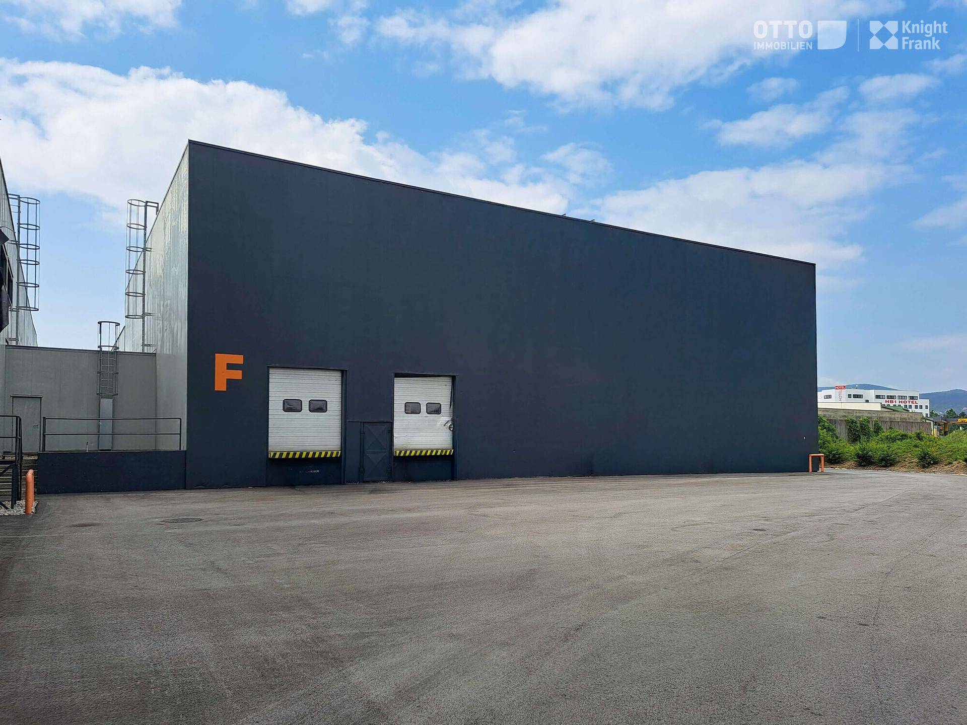 Seitenansicht eines modernen Industriegebäudes mit dunkelgrauer Fassade und zwei kleineren Rolltoren.