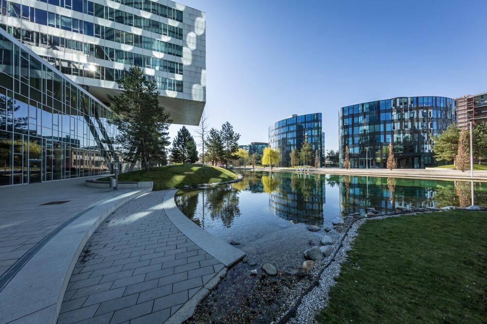 Architektonisch anspruchsvolle Bürogebäude mit Glasfassaden und einem überhängenden Element am Wasserbecken.