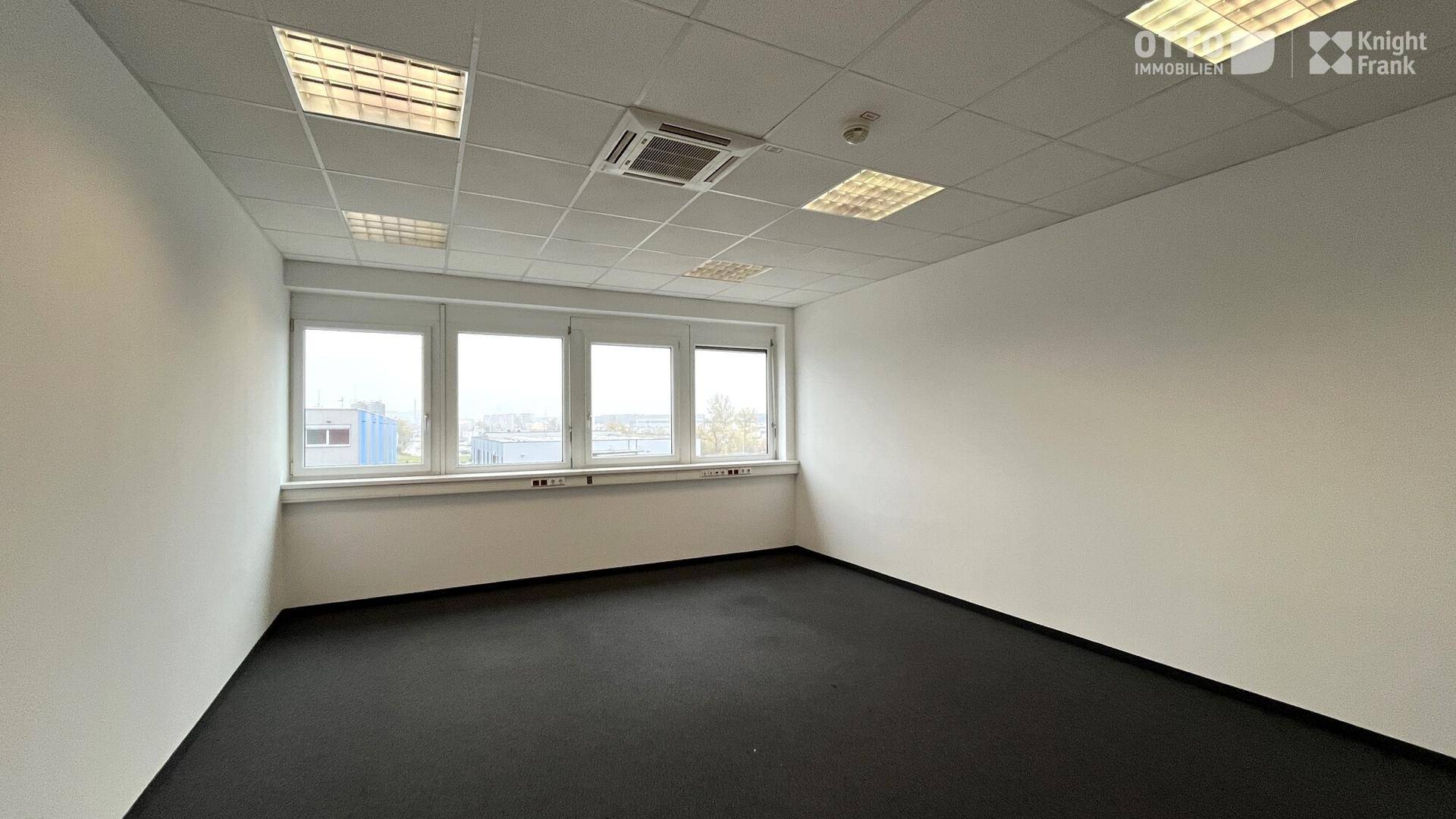 Helles Büro mit großen Fenstern, Teppichboden und abgehängter Decke mit integrierter Beleuchtung.