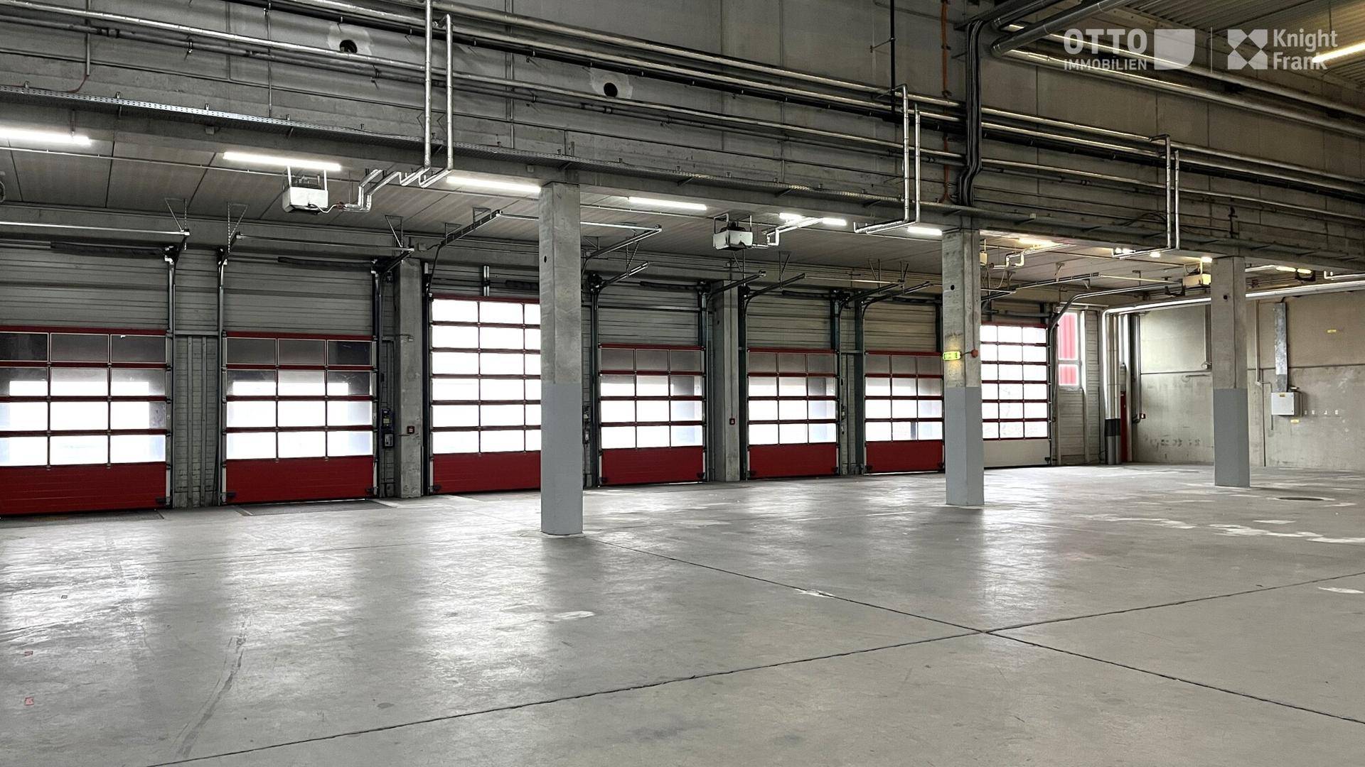 Innenansicht einer Lagerhalle mit vielen Rolltoren, Betonboden und sichtbaren Stützpfeilern.