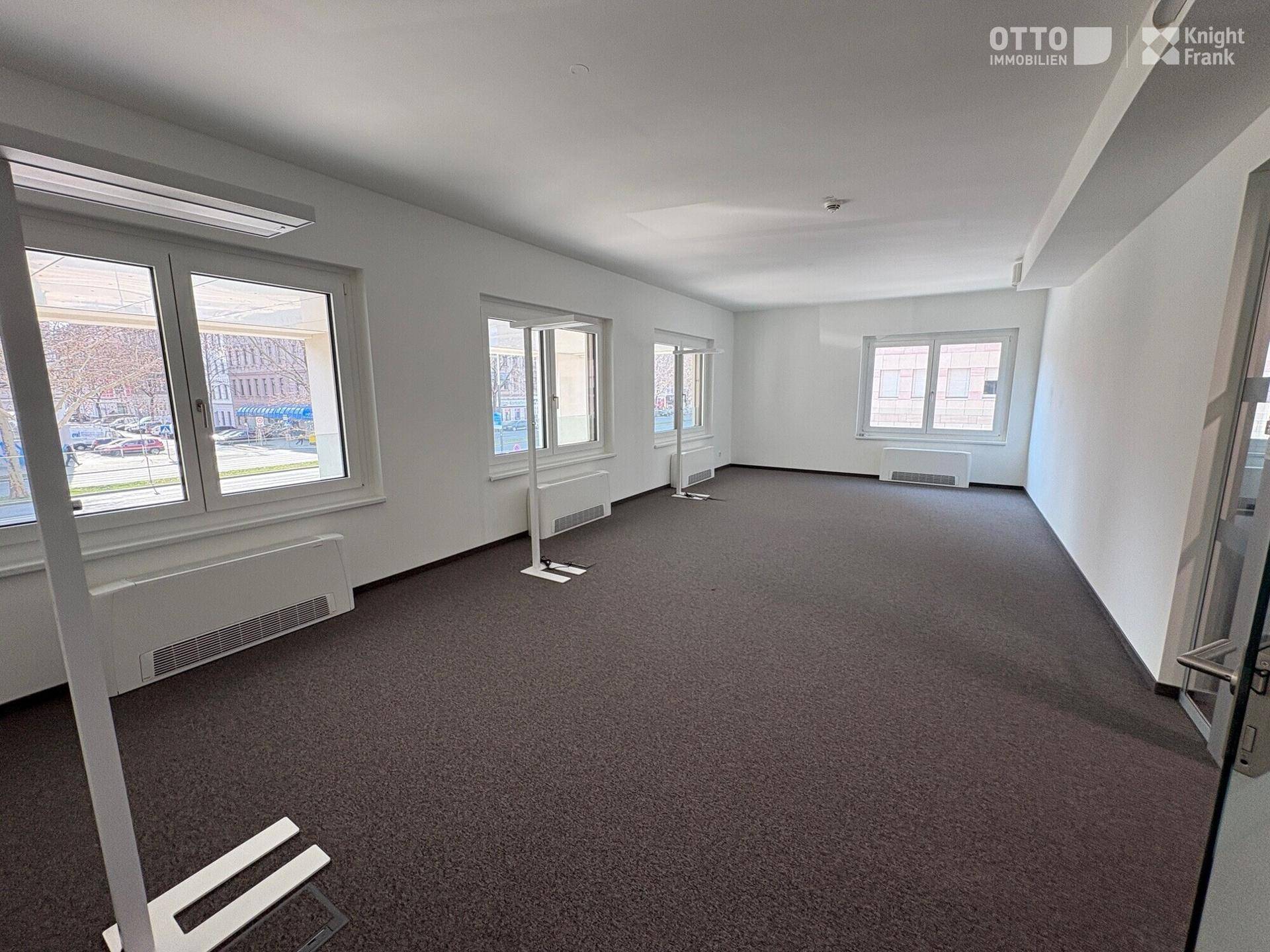 Leeres Büro mit Teppichboden, mehreren Fenstern und Heizkörpern darunter.