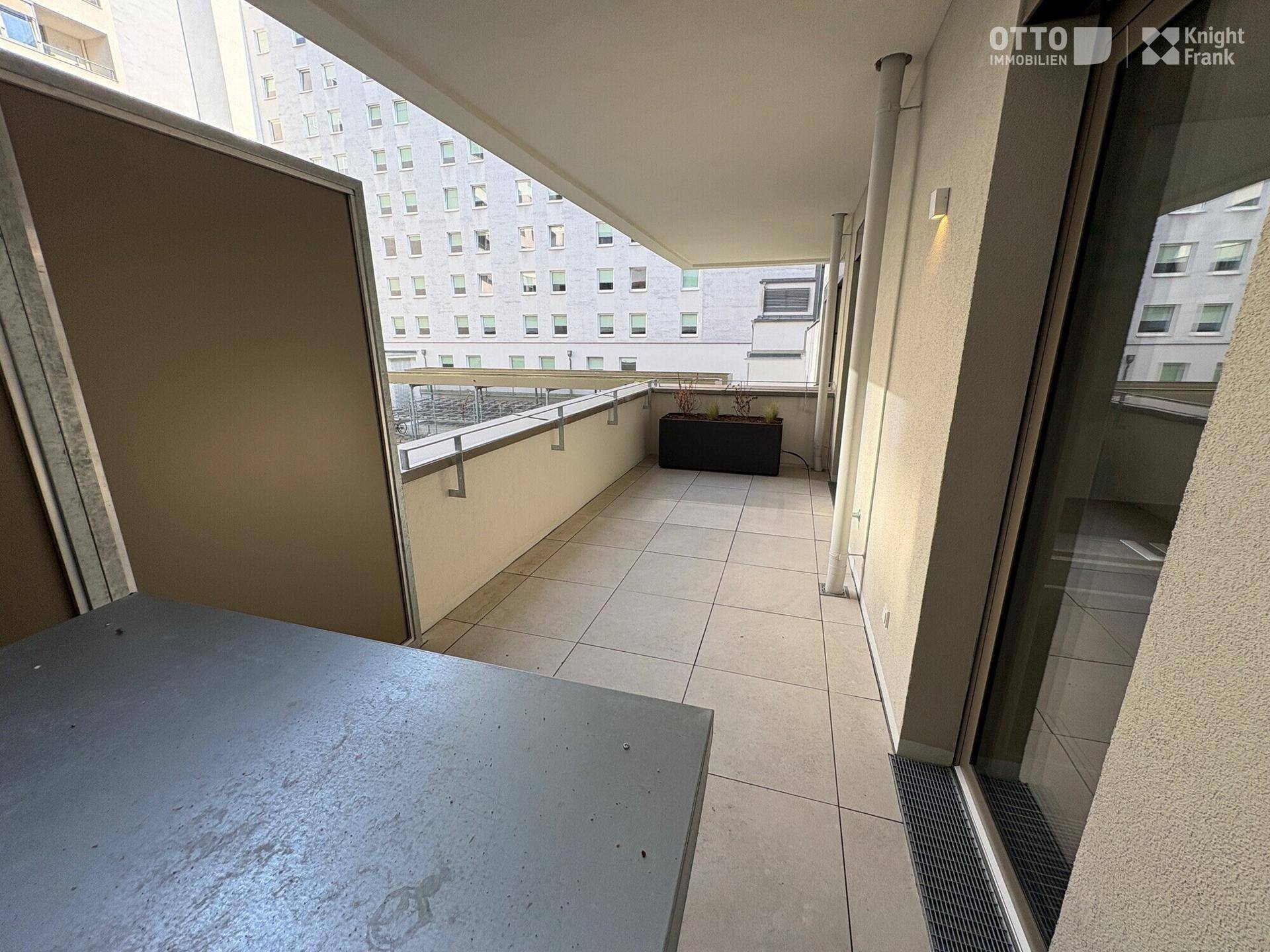 Geräumiger Balkon mit Fliesenboden und Blick auf umliegende Gebäude, ideal zum Entspannen.