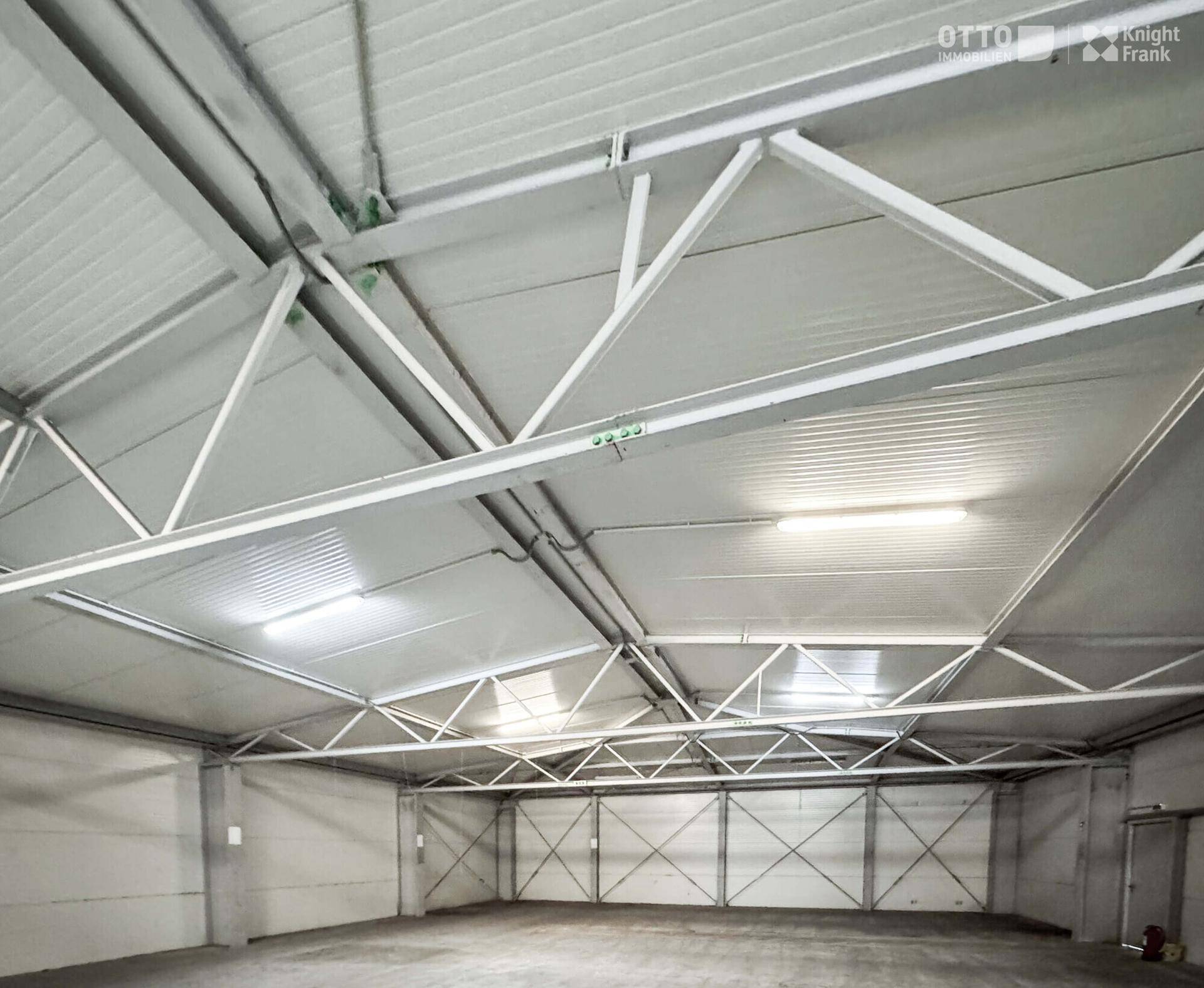 Weitläufige Lagerhalle mit hoher Deckenkonstruktion aus Metall und integrierter Beleuchtung.