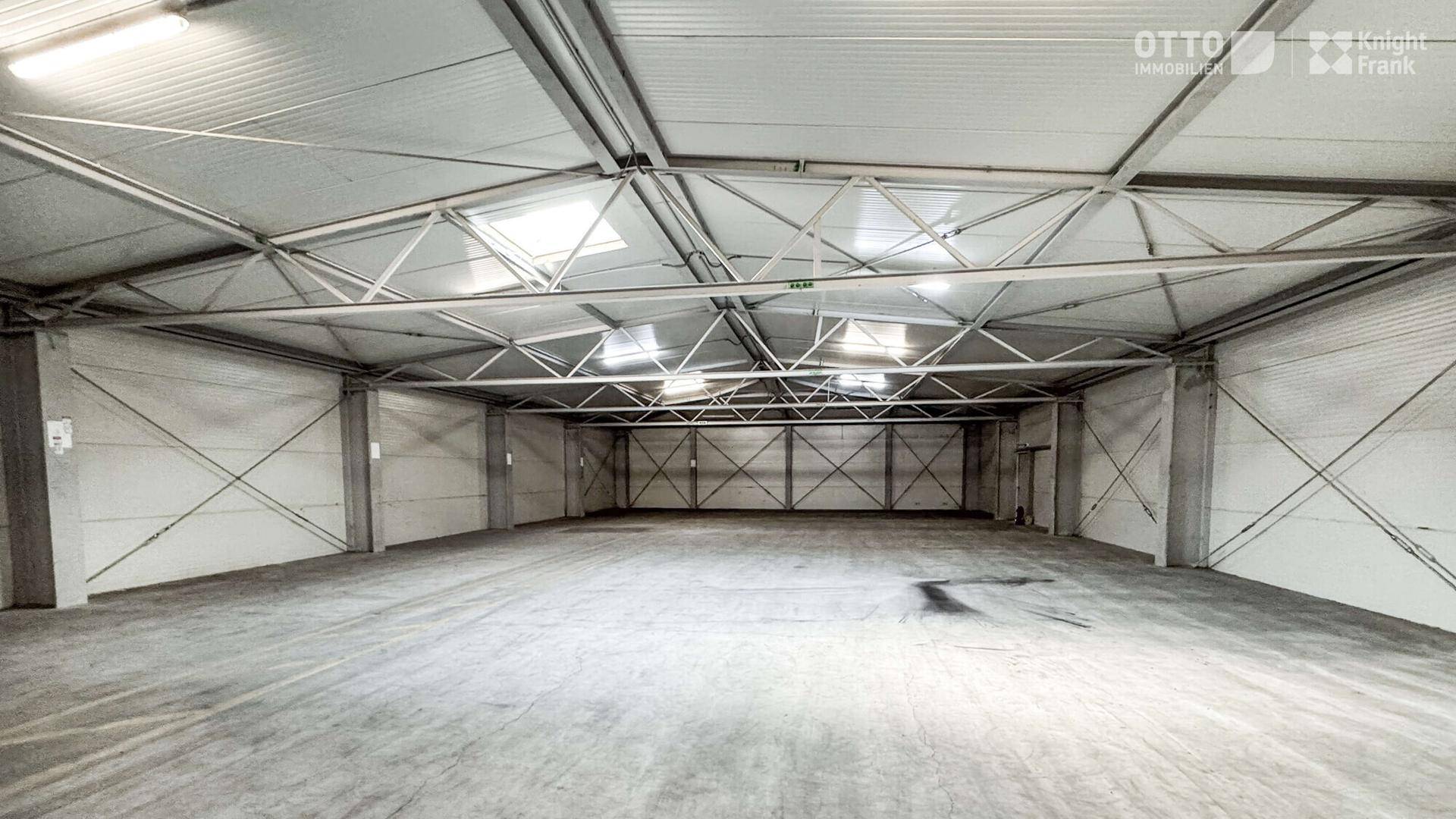 Geräumige, leere Lagerhalle mit Betonboden, hohen Decken und natürlichem Lichteinfall durch Oberlichter.