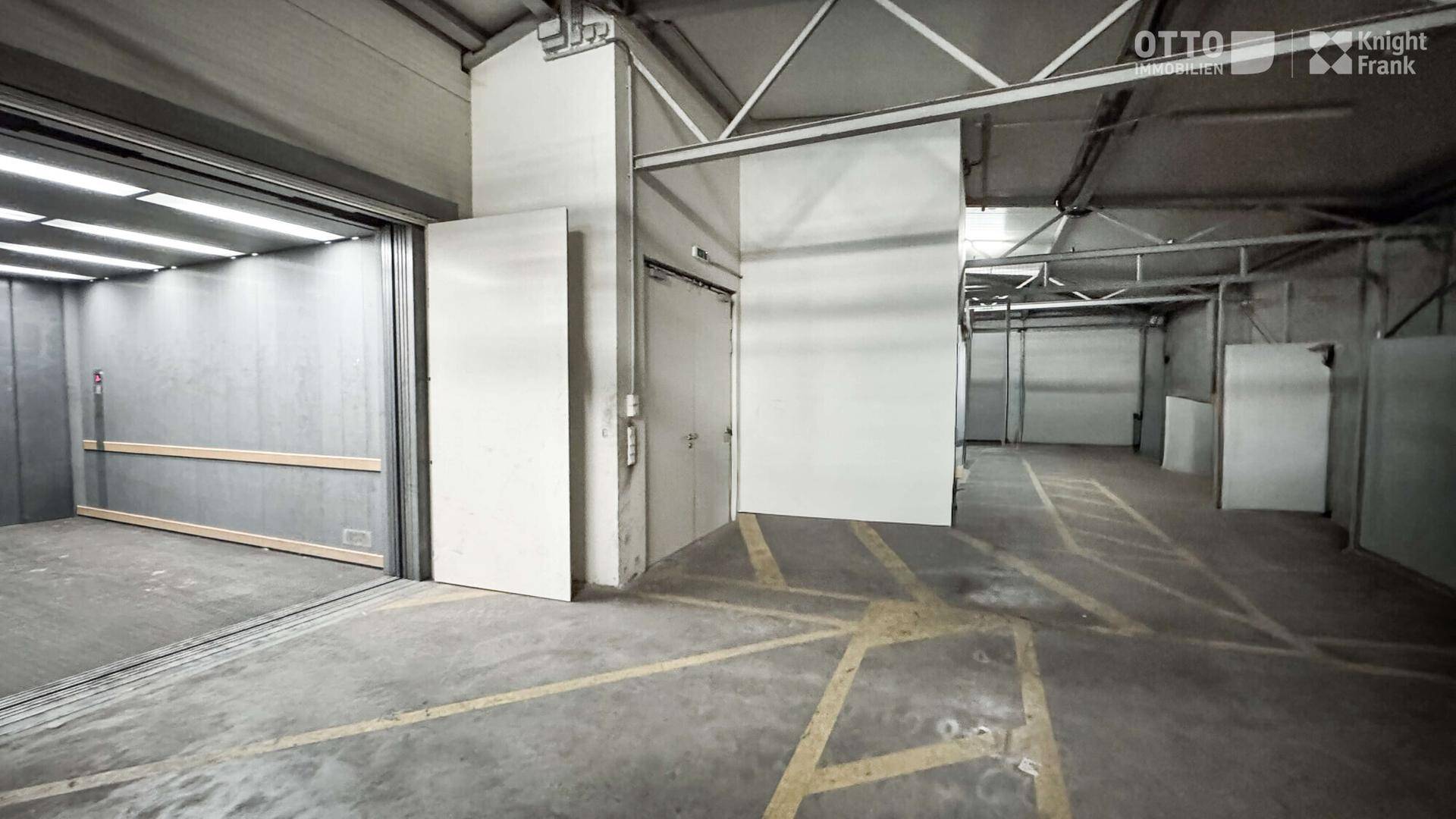 Geräumige Lagerhalle mit Betonboden, mehreren Zugängen und einem großen Lastenaufzug für Logistikzwecke.